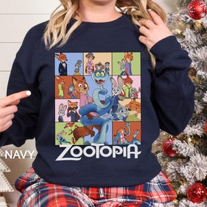 May include: Navy blue sweatshirt featuring a colorful graphic of characters from the animated film "Zootopia." The design includes various animal characters in a grid pattern, with the word "ZOOTOPIA" in white block letters. The word "NAVY" is printed on the left side.