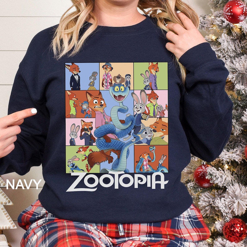 May include: Navy blue sweatshirt featuring a colorful graphic of characters from the animated film "Zootopia." The design includes various animal characters in a grid pattern, with the word "ZOOTOPIA" in white block letters. The word "NAVY" is printed on the left side.