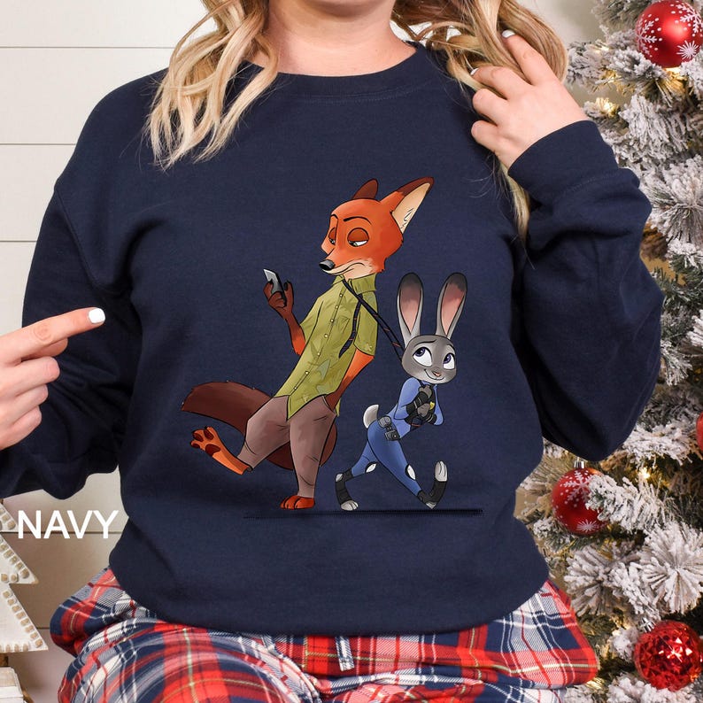 May include: Navy blue sweatshirt featuring a cartoon illustration of Nick Wilde and Judy Hopps from Zootopia. Nick is depicted as a fox in a green shirt and Judy as a rabbit in a blue police uniform. The word "NAVY" is printed on the left side.