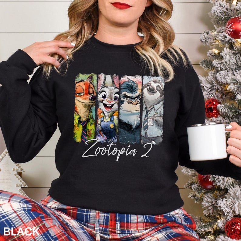 Puede incluir: Sudadera negra con un gr&aacute;fico colorido de personajes de Zootopia 2. El dise&ntilde;o incluye a Nick Wilde, Judy Hopps y otros personajes. El texto "Zootopia 2" est&aacute; escrito en cursiva debajo de los personajes. La palabra "BLACK" est&aacute; impresa en la parte inferior.