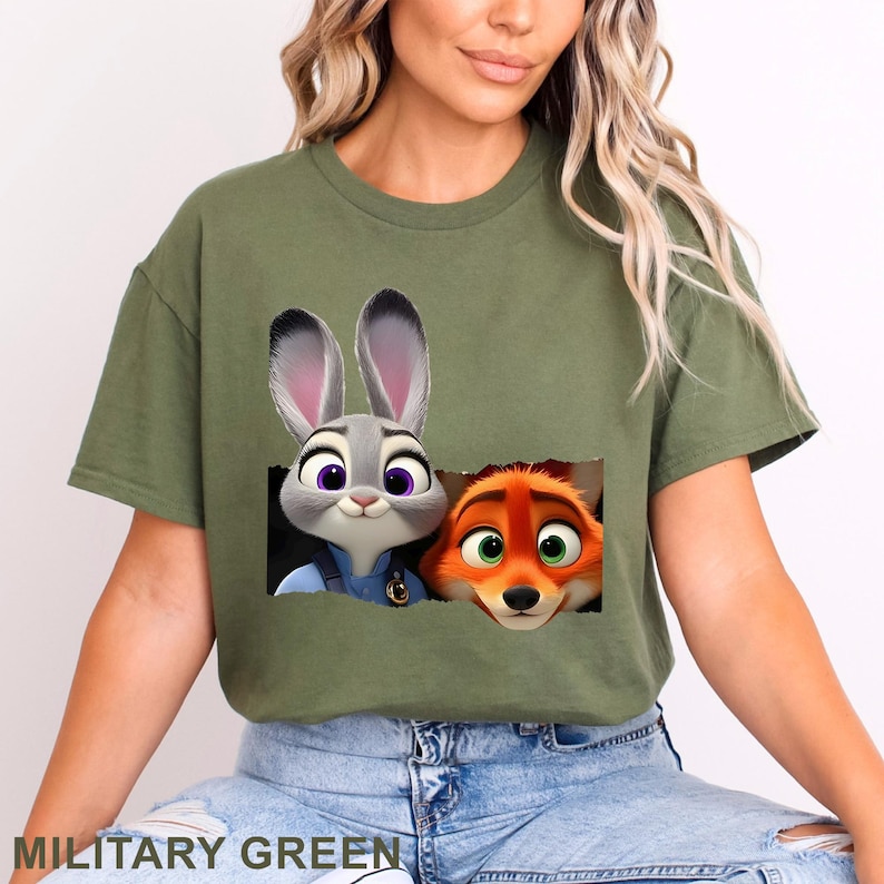 May include: Military green t-shirt featuring a graphic of Judy Hopps and Nick Wilde from Zootopia. The cartoon characters are in a rectangular cutout. The text "MILITARY GREEN" is at the bottom of the shirt.