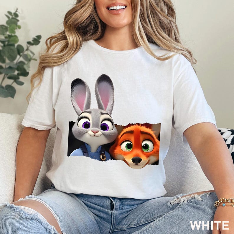 May include: White t-shirt featuring a graphic of Judy Hopps and Nick Wilde from the animated movie Zootopia. The characters are depicted in a torn paper effect. The word "WHITE" is printed at the bottom right.