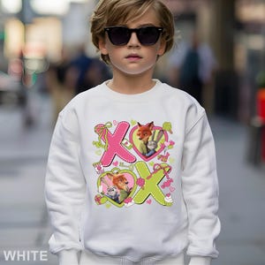 Peut inclure: Sweat-shirt blanc avec des personnages de Zootopie, dont Nick Wilde et Judy Hopps, avec le texte "XO" en rose et vert. Le motif comprend des formes de c&oelig;ur et des &eacute;l&eacute;ments d&eacute;coratifs. Le mot "WHITE" est imprim&eacute; en bas.