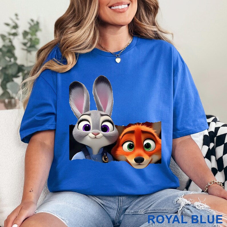 May include: Royal blue t-shirt featuring a graphic of a gray bunny and an orange fox. The bunny has purple eyes and the fox has green eyes. The text "ROYAL BLUE" is at the bottom of the shirt.
