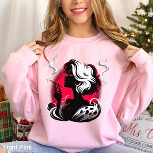 Op de afbeelding: Lichtroze sweatshirt met een zwart-wit silhouet van een vrouw die een sigaret rookt, tegen een rode cirkel. Het ontwerp bevat gestileerde rook en een zwart-witte werveling aan de onderkant.