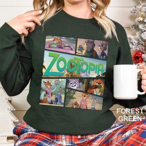 May include: Forest green sweatshirt featuring a comic strip design with characters and the title "Zootopia" in teal. The sweatshirt has long sleeves and is made of a soft material. The words "Forest Green" are printed on the bottom right.