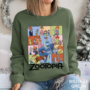 May include: Military green sweatshirt featuring a colorful graphic from the animated film "Zootopia." The design includes various characters in a grid layout, with the film's title in black at the bottom. The sweatshirt is made of a soft material.