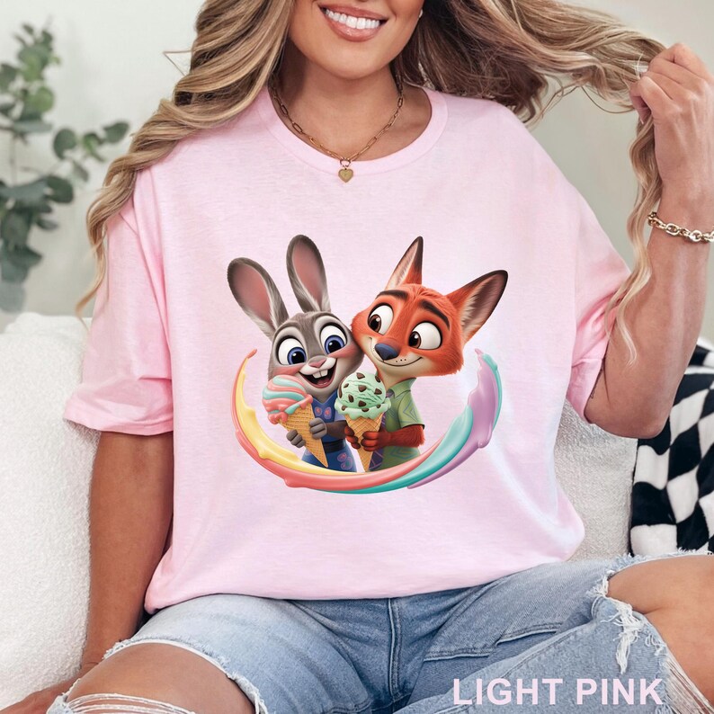 May include: Light pink t-shirt featuring a colorful graphic of a bunny and fox holding ice cream cones. The characters are surrounded by a rainbow swirl. The text "LIGHT PINK" is at the bottom of the shirt.
