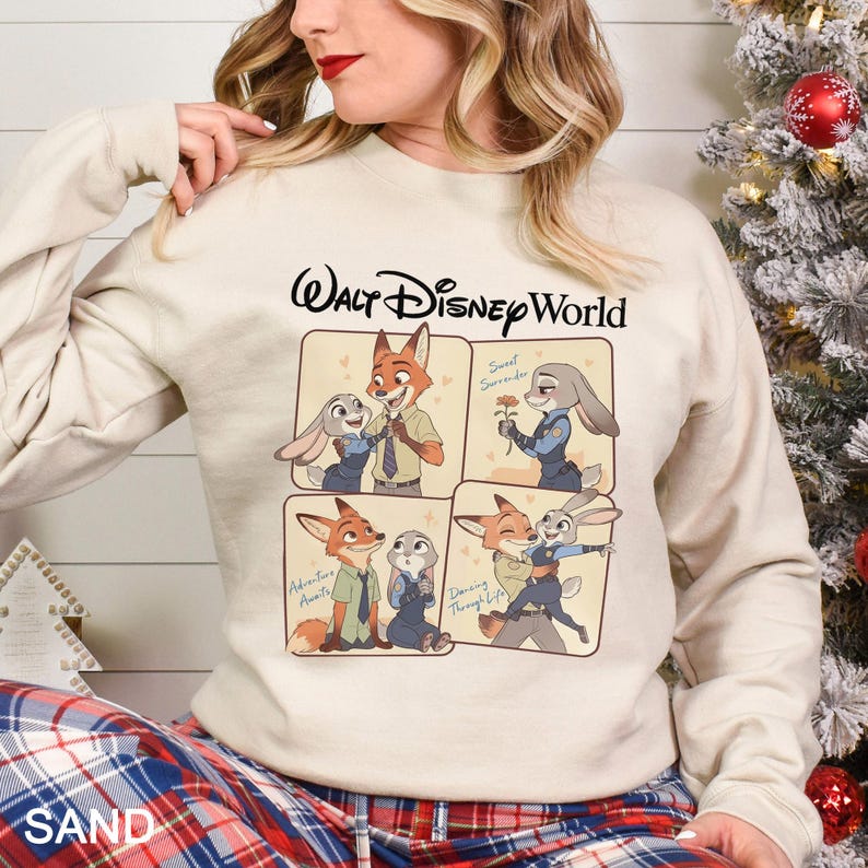 May include: A sand-coloured sweatshirt with the Walt Disney World logo and four panels of Zootopia characters. The panels show Nick Wilde and Judy Hopps in different poses. The sweatshirt is a long-sleeved crew neck.