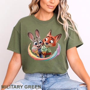May include: Military green t-shirt featuring a colorful graphic of Judy Hopps and Nick Wilde from Zootopia, holding ice cream cones. The design includes a rainbow swirl. The text "MILITARY GREEN" is at the bottom.