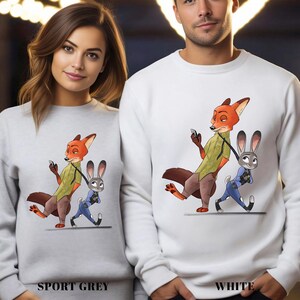 May include: Sport grey and white sweatshirts featuring a cartoon fox and bunny design. The fox is wearing a green shirt and holding a phone, while the bunny is in a police uniform. The text "SPORT GREY" and "WHITE" are printed at the bottom.