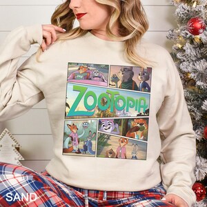 May include: Sand-colored sweatshirt featuring a colorful comic strip design from the animated movie Zootopia. The graphic includes various characters and the movie's title in large, green and blue letters. The sweatshirt is a long-sleeved, casual style.