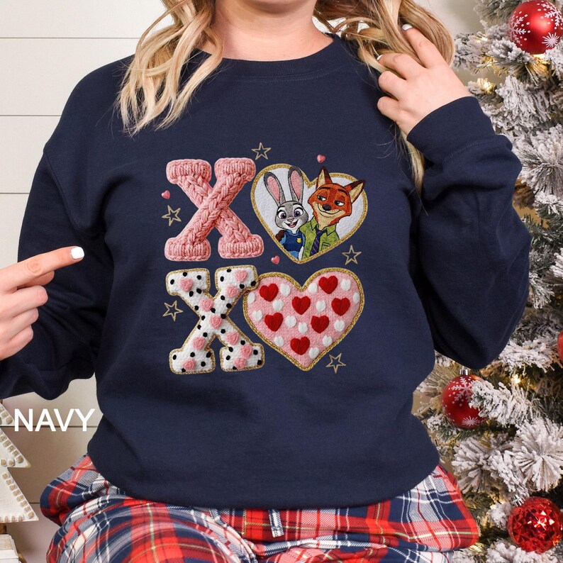 May include: Navy blue sweatshirt with embroidered "XO" design. Features a pink knitted "X", a heart with Judy Hopps and Nick Wilde, and a heart with red polka dots. Gold star accents and the word "NAVY" are also visible.