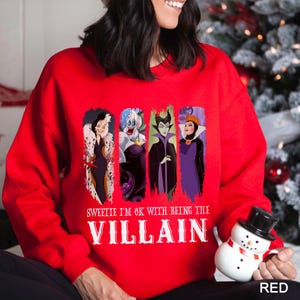 May include: A red sweatshirt featuring four cartoon villain characters. The sweatshirt has the text "Sweetie I'm OK with being the Villain" in white. The word "RED" is printed in the bottom right corner.