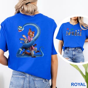 K&ouml;nnte beinhalten: K&ouml;nigsblaues T-Shirt mit einem Cartoon-Motiv einer Schlange, die sich um einen Fuchs und ein Kaninchen windet. Der Fuchs tr&auml;gt einen rosa Anzug und das Kaninchen ein blaues Outfit. Die Grafik befindet sich auf der R&uuml;ckseite des Shirts.