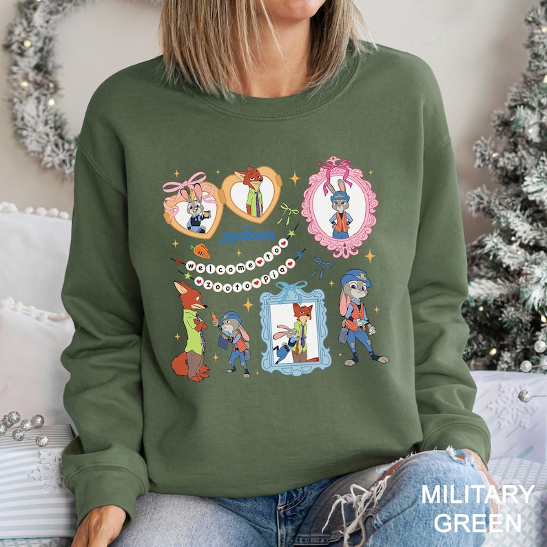 以下が含まれることがあります： ズートピアの漫画のキャラクターが描かれたオリーブグリーンのスウェットシャツ。デザインには、ジュディ・ホップスとニック・ワイルドの額縁入りポートレート、そして「Welcome to Zootopia」というテキストがバナーに描かれています。スウェットシャツには「MILITARY GREEN」と書かれています。