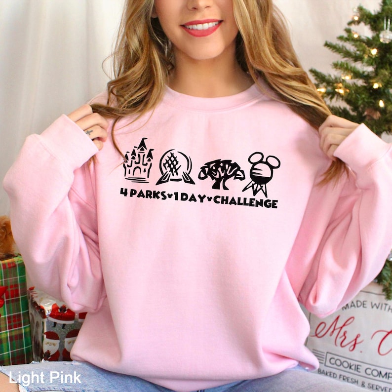 May include: Light pink sweatshirt with a black graphic featuring four iconic park symbols and the text "4 PARKS 1 DAY CHALLENGE". The sweatshirt is a light pink color.
