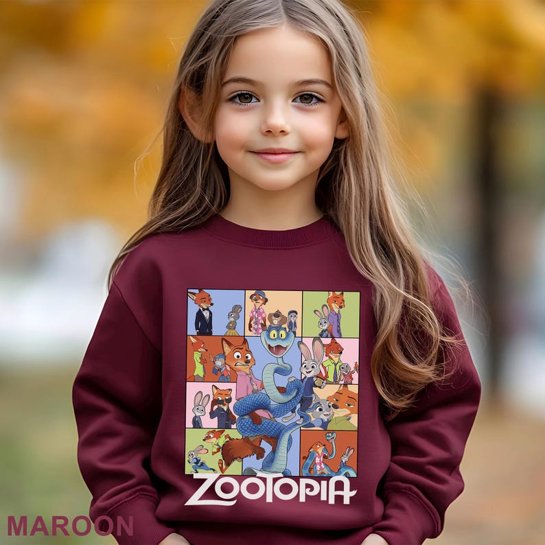 May include: A maroon sweatshirt featuring a colorful graphic of characters from the animated film "Zootopia." The design includes various animal characters in a grid pattern, with the word "Zootopia" in white at the bottom. The word "MAROON" is at the bottom left.