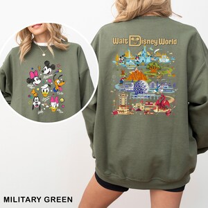 May include: Military green sweatshirt featuring Disney characters Mickey Mouse, Minnie Mouse, Donald Duck, Daisy Duck, and Goofy. The back of the sweatshirt displays a colorful graphic of Walt Disney World with the text "Walt Disney World".