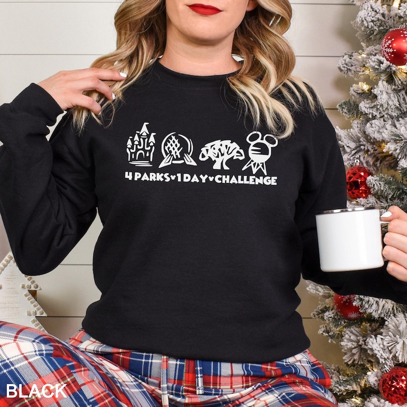 May include: Black crewneck sweatshirt with white graphic text and icons. The text reads "4 Parks 1 Day Challenge" with icons of a castle, sphere, tree, and Mickey Mouse. The word "BLACK" is printed at the bottom left.