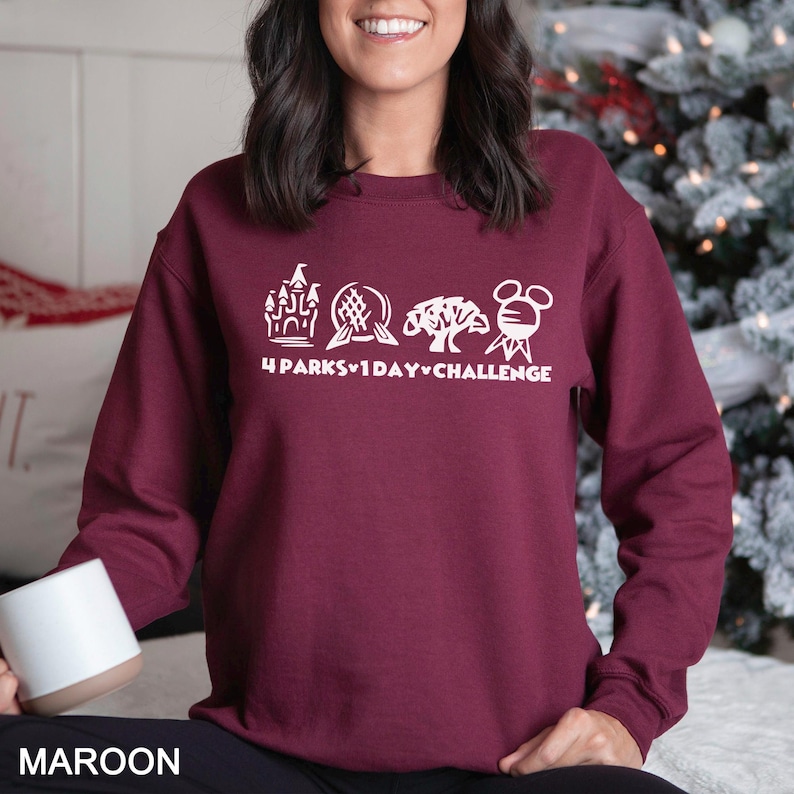 May include: Maroon sweatshirt with white graphic of four theme park icons and the text "4 Parks 1 Day Challenge". The sweatshirt is a crew neck style and is made of a soft material. The word "MAROON" is printed at the bottom.
