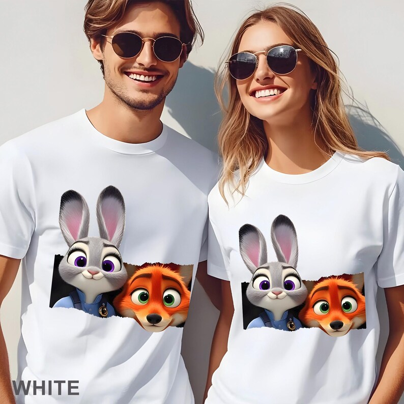 May include: White t-shirts featuring a graphic of Judy Hopps and Nick Wilde from Zootopia. The cartoon characters are depicted emerging from a torn-paper effect. The word "WHITE" is printed at the bottom of the shirt.