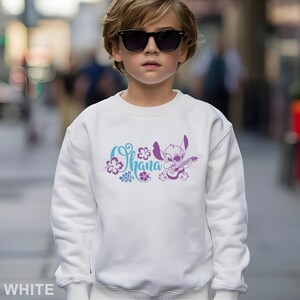 May include: White sweatshirt featuring a graphic of Stitch playing a guitar, with the word "Ohana" in a floral design. The design is in shades of blue and purple. The sweatshirt is a casual style.
