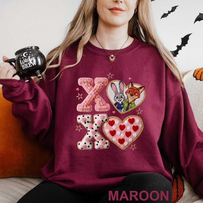 May include: Maroon sweatshirt featuring embroidered "XO" letters and heart designs. One heart contains Judy Hopps and Nick Wilde from Zootopia. The other heart is filled with red hearts. The word "MAROON" is at the bottom.