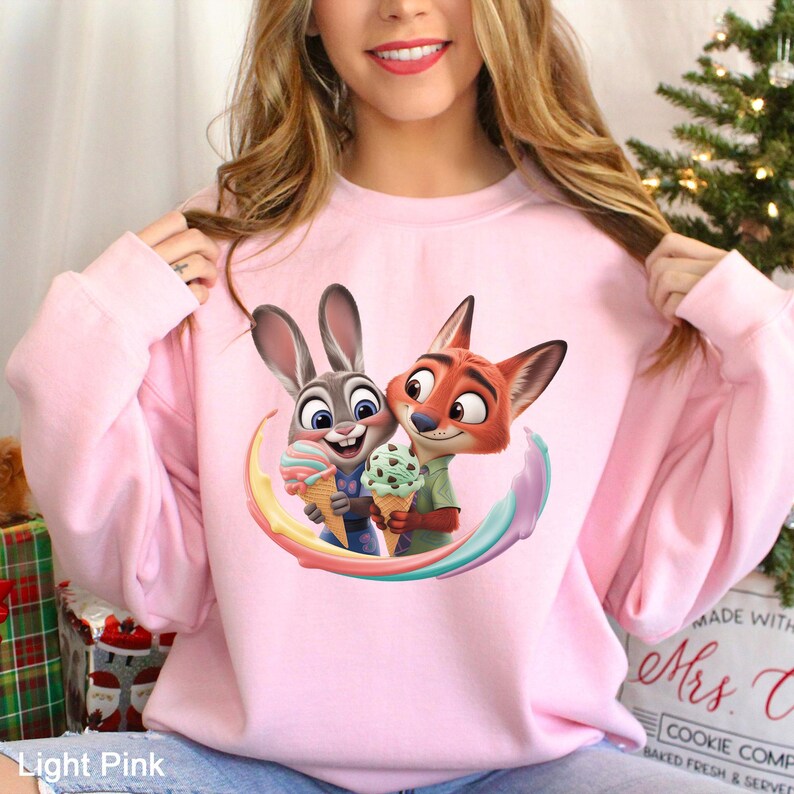 May include: Light pink sweatshirt featuring a cartoon image of a bunny and a fox holding ice cream cones. The bunny and fox are surrounded by a rainbow arc. The text "Light Pink" is at the bottom of the image.