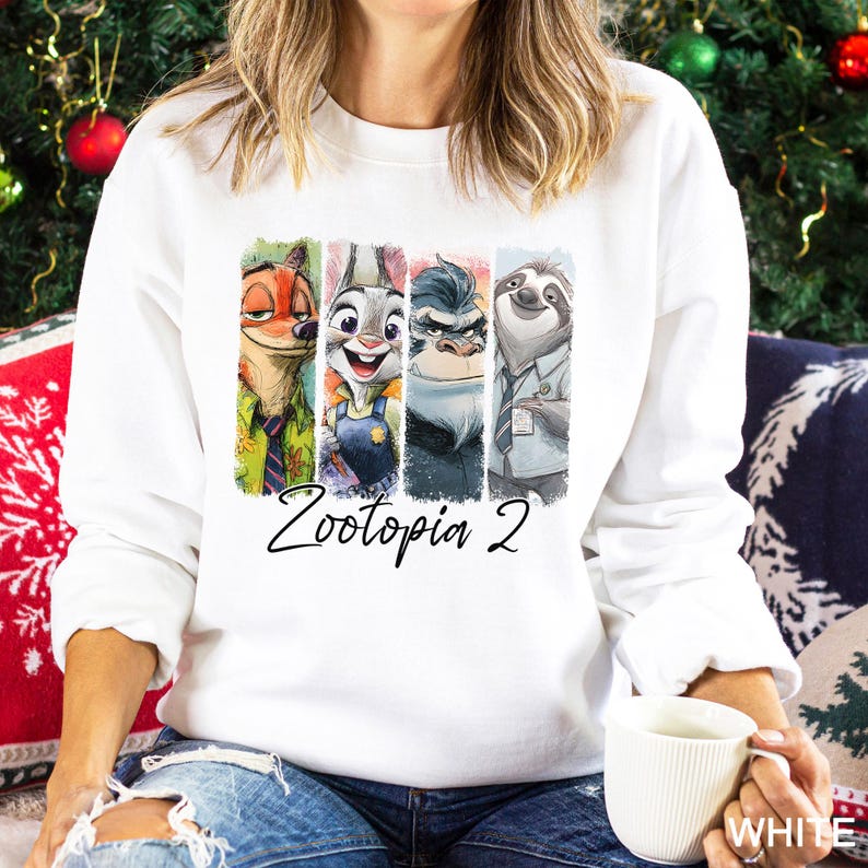 Puede incluir: Sudadera blanca con un dise&ntilde;o colorido de personajes de Zootopia 2. El dise&ntilde;o incluye a Nick Wilde, Judy Hopps, el Jefe Bogo y Flash. El texto "Zootopia 2" est&aacute; escrito debajo. Es una prenda de vestir informal.