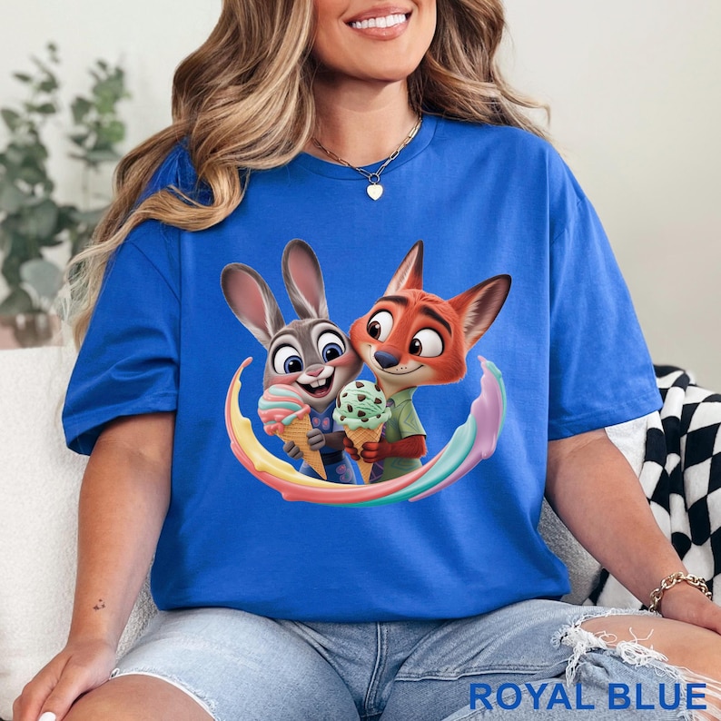 May include: Royal blue t-shirt featuring a colorful graphic of cartoon characters Judy Hopps and Nick Wilde from Zootopia, holding ice cream cones. The shirt has a crew neck and short sleeves. The text "ROYAL BLUE" is printed at the bottom.