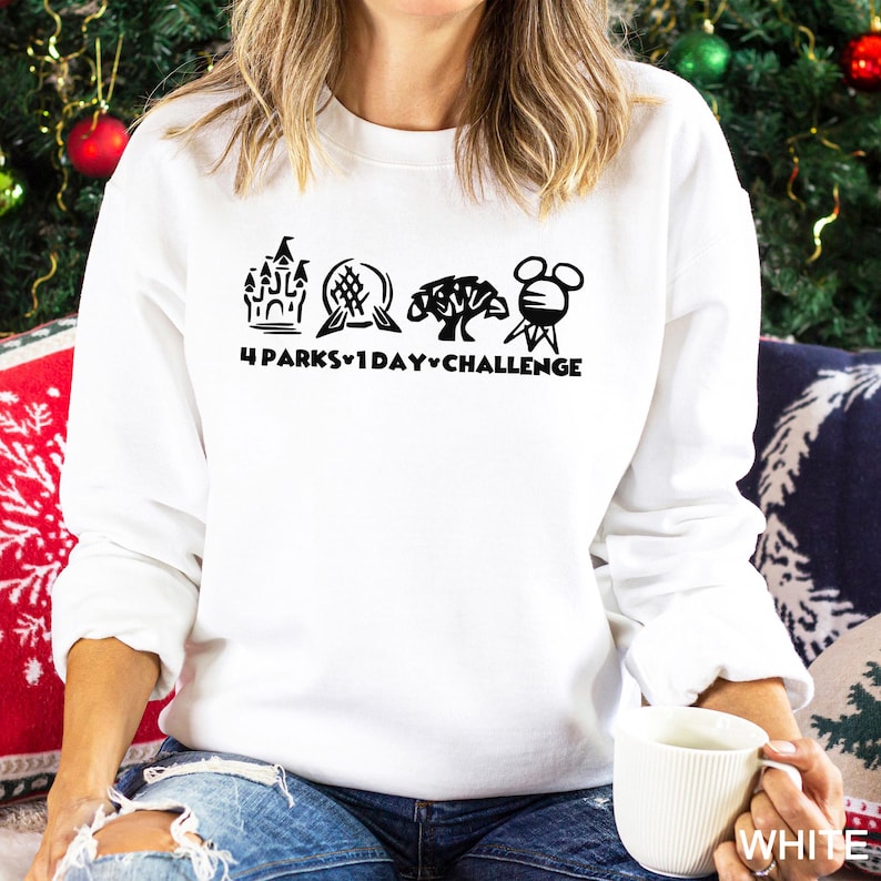 May include: White sweatshirt with a black graphic featuring four theme park icons and the text "4 Parks 1 Day Challenge." The sweatshirt is a crew neck style and is being held by a person.