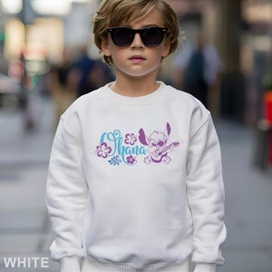 May include: White sweatshirt featuring a graphic of Stitch playing a guitar, with the word "Ohana" in a floral design. The design is in shades of blue and purple. The sweatshirt is a casual style.