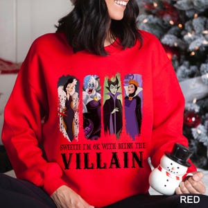May include: Red sweatshirt featuring four cartoon villain characters. The text "Sweetie I'm OK with being the Villain" is printed below the characters. The word "RED" is printed in the bottom right corner.