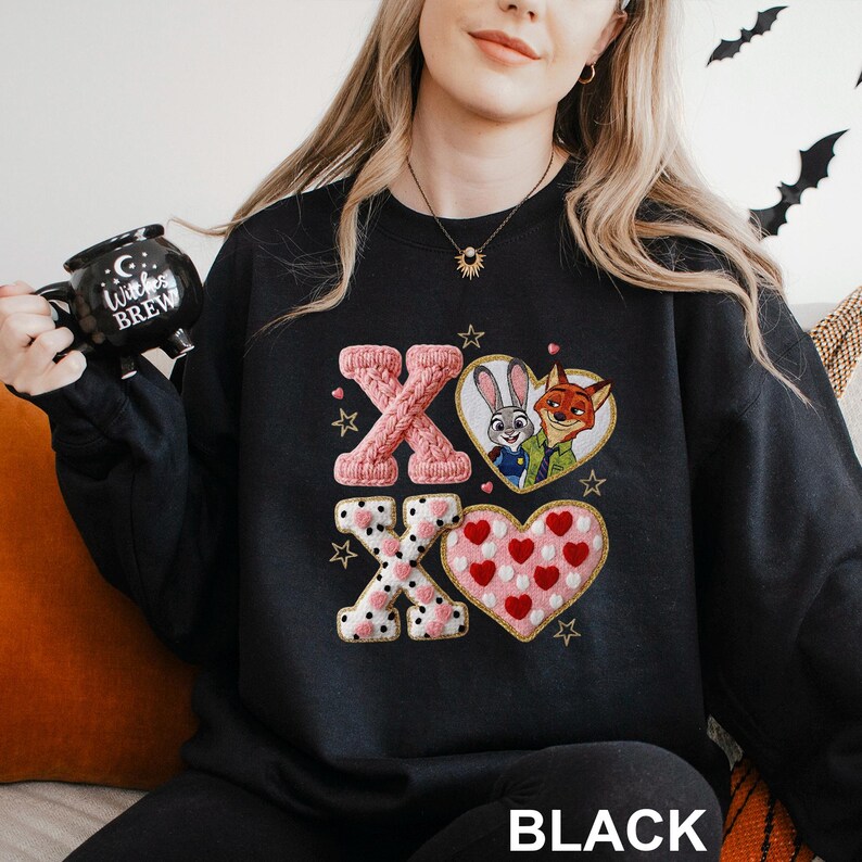 May include: Black sweatshirt featuring the letters "XO" in pink and white, with heart and star accents. The design includes a heart with cartoon characters and a heart filled with red hearts. The word "BLACK" is at the bottom.