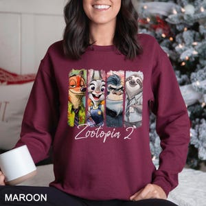 Puede incluir: Sudadera granate con personajes de Zootopia. El dise&ntilde;o incluye a Nick Wilde, Judy Hopps, el Jefe Bogo y Flash, con el texto "Zootopia 2" en escritura blanca. La sudadera es de color granate liso.