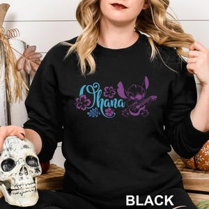 May include: Black sweatshirt featuring the word "Ohana" in blue and purple script, with a cartoon character playing a guitar. The word "BLACK" is printed at the bottom of the sweatshirt.