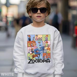 May include: White sweatshirt featuring a colorful graphic of characters from the animated movie "Zootopia." The design includes various animal characters in a grid pattern, with the movie title in black at the bottom.