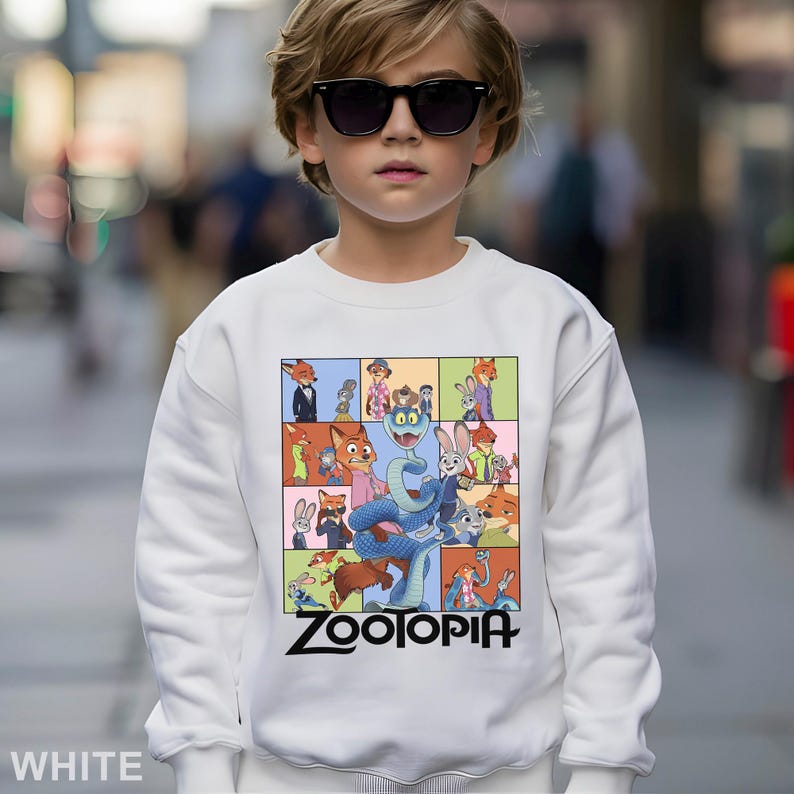 May include: White sweatshirt featuring a colorful graphic of characters from the animated movie "Zootopia." The design includes various animal characters in a grid pattern, with the movie title in black at the bottom.