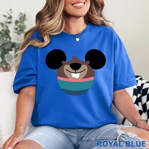May include: Royal blue t-shirt featuring a cartoon character design. The graphic includes a brown face with black ears, a pink and teal striped design, and a white tooth. The text "ROYAL BLUE" is at the bottom of the image.