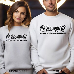 May include: Sport grey and white sweatshirts with a black graphic design featuring a castle, globe, tree, and Mickey Mouse head. The text "4 PARKS 1 DAY CHALLENGE" is below the graphics. The sport grey sweatshirt is labeled "SPORT GREY" and the white sweatshirt is labeled "WHITE".