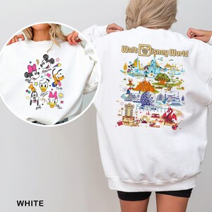May include: White sweatshirt featuring a colorful graphic of Disney characters on the front and a Walt Disney World map design on the back. The front graphic includes Mickey, Minnie, Donald, Daisy, Goofy, and Pluto. The text "WHITE" is at the bottom.