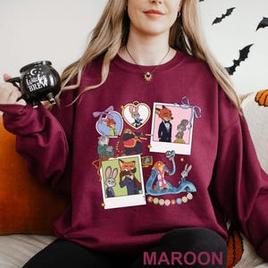 May include: Maroon sweatshirt featuring cartoon characters from Zootopia in polaroid-style frames. The design includes Judy Hopps and Nick Wilde, along with other characters. The word "MAROON" is printed at the bottom.