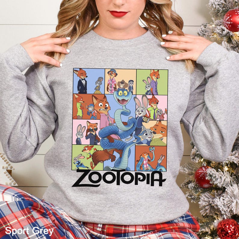 May include: Sport grey sweatshirt featuring a colorful Zootopia graphic. The graphic includes various characters from the animated film, such as Nick Wilde, Judy Hopps, and others, in a grid-like design. The word "Zootopia" is printed in black.