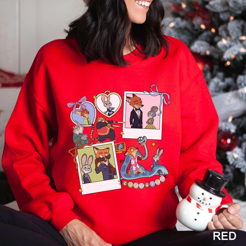 May include: A red sweatshirt featuring a collage of Zootopia characters in various poses, including Nick Wilde and Judy Hopps. The word "Zootopia" is written in a circle. The sweatshirt is a festive holiday item.