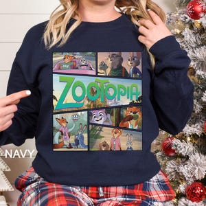 May include: Navy blue sweatshirt featuring a colorful graphic of scenes from the animated movie "Zootopia." The word "Zootopia" is displayed in large, green and blue letters. The word "NAVY" is printed on the bottom left of the sweatshirt.
