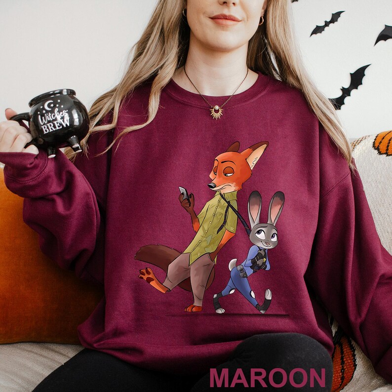 May include: Maroon sweatshirt featuring a cartoon fox and bunny character design. The fox is holding a phone, and the bunny is in a police uniform. The word "MAROON" is printed at the bottom. The sweatshirt is a crew neck style.