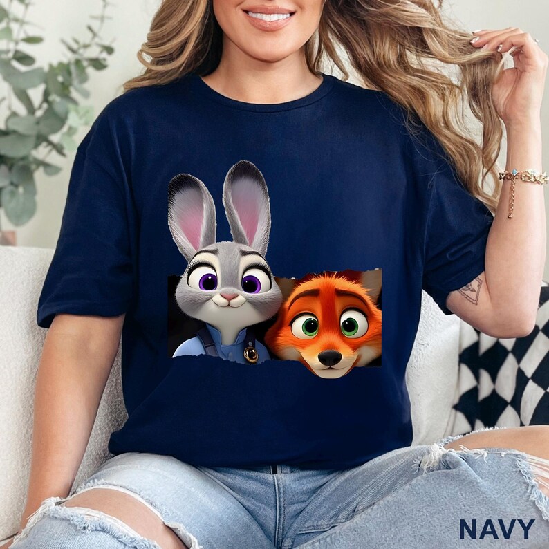 May include: Navy blue t-shirt featuring a graphic of Judy Hopps and Nick Wilde from Zootopia. The cartoon characters are in a pocket-like design. The word "NAVY" is printed at the bottom of the shirt.