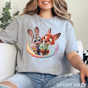 May include: Sport grey t-shirt featuring a colorful graphic of two cartoon characters, a rabbit and a fox, holding ice cream cones. The characters are surrounded by a rainbow arc. The text "SPORT GREY" is printed at the bottom right.