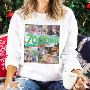 May include: White sweatshirt featuring a comic strip design with characters and the title "Zootopia" in green. The design includes various scenes from the animated movie. The sweatshirt is long-sleeved and has a crew neck.